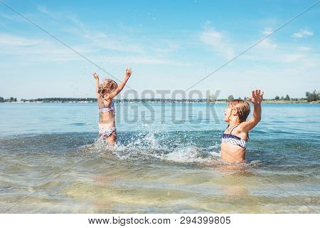 Two Little Sister Girls Fooling Around In The Calm Sea Waves Splashing Water To Each Other. Family V