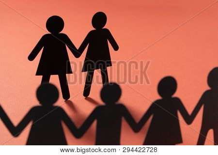 Black paper figure of a female couple in front of a crowd of paper people holding hands on vivid red background. Social movement, minorities, same-sex marriage concept.