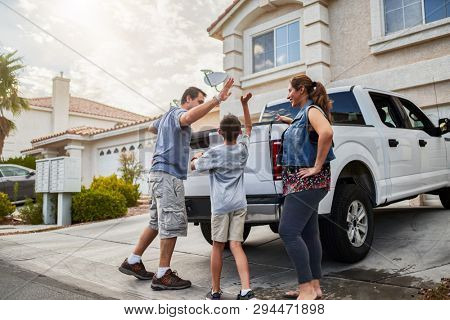 hispanic family loading luggage into back of pickup truck in front of house for travel