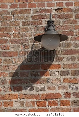 Old Fashioned Metal And Globe Light Fitting Outdoor On Old Brick Wall With Daytime Shadow