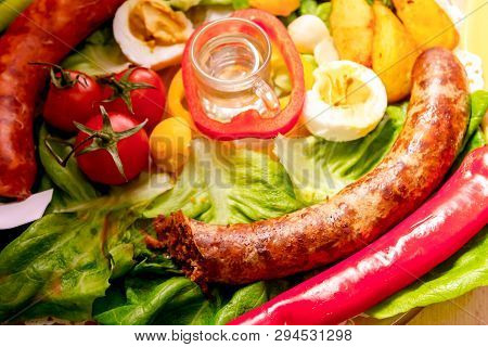 Decorated Sausages With Fresh Vegetables, Eggs And Glass Of Brandy Are Exposed On Traditional Sausag