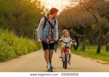 Active Sports Family Father On Scooter With Kids Outside, A Little Girl On The Bike
