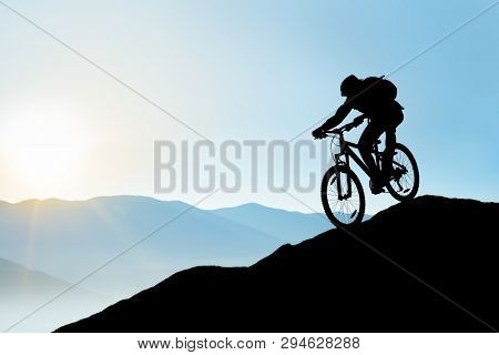 Silhouette of Cyclist Riding the Bike in the Beautiful Mountains Down the Rock on the Sunrise Sky Background. Extreme Sport and Enduro Biking Concept.