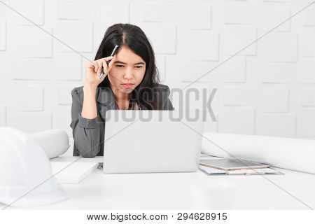 Shot Of Young Beautiful Asian Architect In Business Casual, Pen In Hand Looking At Laptop Screen, Re