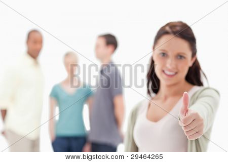 Close-up of a woman with focus on her thumbs-up with friends in background