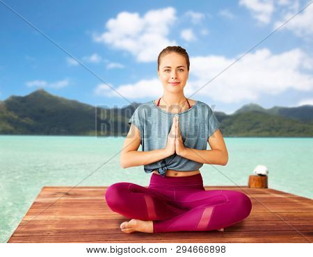 mindfulness, spirituality and healthy lifestyle concept - woman doing outdoor yoga and meditating in lotus pose on wooden pier over ocean in french polynesia background