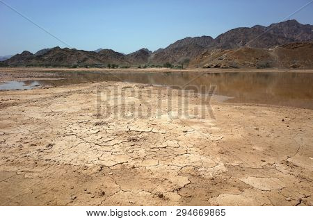 Desert landscape with cracked mud, puddle and dry mountains in Fujairah, United Arab Emirates