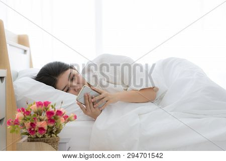 Young And Beautiful Asian Woman Sleep In Bed And Using Smartphone After Awake With Copy Space On Top