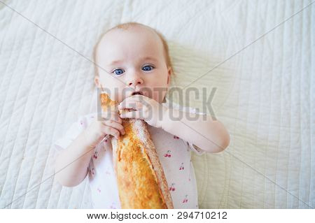 Six Months Old Baby Girl Eating Traditional French Bread (baguette). Introducing Solids To Infant Ki