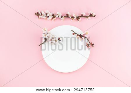 White Plate On Pink Background With Spring Blooms. Festive Background For Your Text. Flat Lay Style.