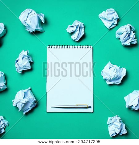White Notebook With Pen On A Green Background Among Paper Balls. The Concept Of Generating Ideas, In