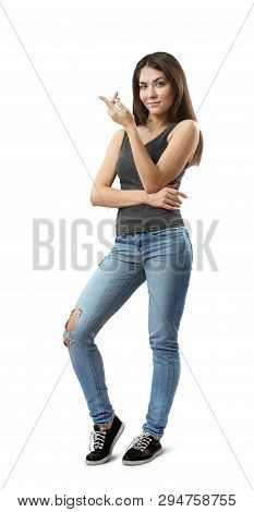 Young Woman In Jeans And Gray Top Standing In Half-turn With Right Arm Across Belly And Left Arm Ben
