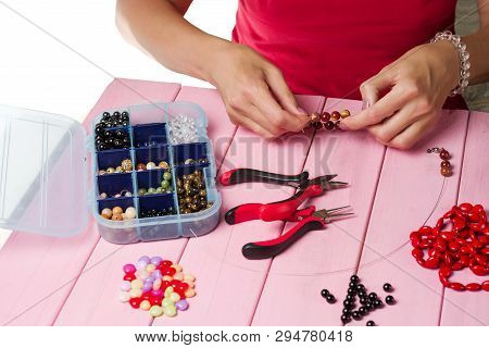 Jewelry Making. Making Bracelet Of Colorful Beads. Female Hands With A Tool On A Pink Background.