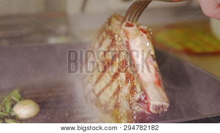 Unrecognizable Man Chefs Hands Using Two Forks Are Rotaring A Juicy Beef Steak Wich Roasting With Ro