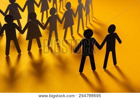 Black paper figure of male couple in front of a crowd of paper people holding hands on orange surface. Social movement, protest, minorities concept.