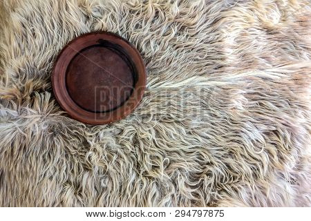 Round Sooty Ceramic Saucer On A Background Of White Goatskin. Rustic Patterns Under Sunlight