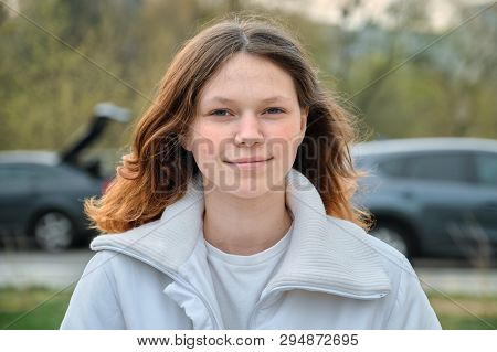 Outdoor Portrait Of Teenager Girl 15 Years Old, Girl Smiling With Long Brown Hair In White Jacket.