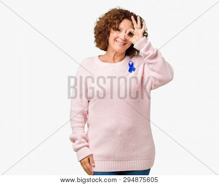 Middle ager senior woman wearing changeable blue color ribbon awareness over isolated background doing ok gesture with hand smiling, eye looking through fingers with happy face.