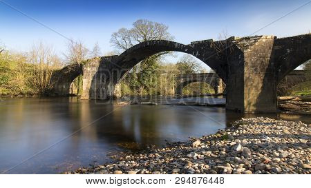 An Old Stone Bridge Over A River Shot With A Long Exposure To Soften The Water.