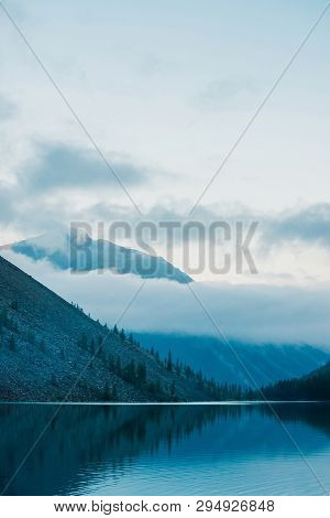 Amazing Silhouettes Of Mountains And Low Clouds Reflected On Mountain Lake. Beautiful Ripples On Wat