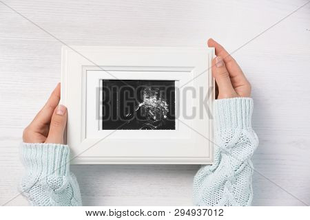 Woman Holding Ultrasound Photo Of Baby Over Wooden Table, Top View