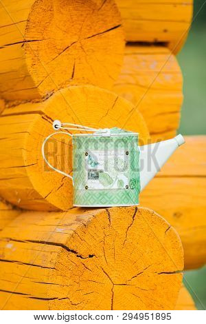 Green Metal Watering Can Stands On The Ledge Of A Yellow Wooden Rustic Log House