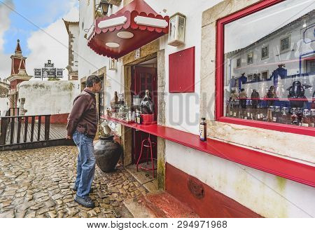 Obidos, Portugal - April 2018: Buying Ginja - Traditional Sour Cherry Liqueur In The Old Town