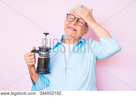 Senior beautiful woman with blue eyes and grey hair holding french coffee maker stressed and frustrated with hand on head, surprised and angry face 
