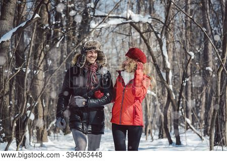 Couple having a winter walk on a chilly cold day in the woods down a path in the snow