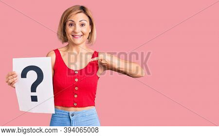 Young blonde woman holding question mark pointing finger to one self smiling happy and proud 