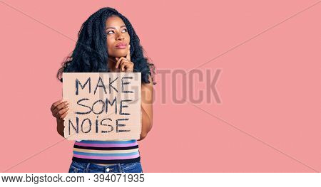 Beautiful african american woman holding make some noise banner serious face thinking about question with hand on chin, thoughtful about confusing idea 
