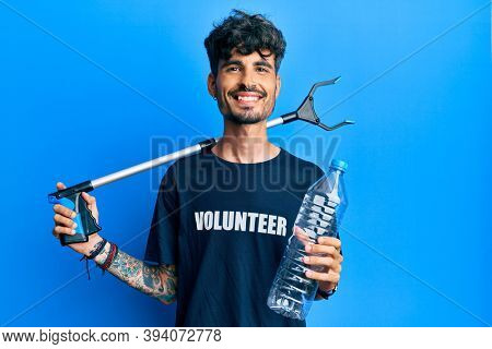 Young hispanic man holding plastic bottle and litter picker to recycle smiling with a happy and cool smile on face. showing teeth. 