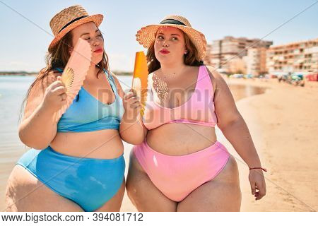 Two plus size overweight sisters twins women using handfan at beach on hoy day of summer