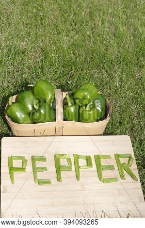 Ripe Green Pepper In Wooden Basket With Word Pepper In Pieces On Wooden Background In Grass With Cop