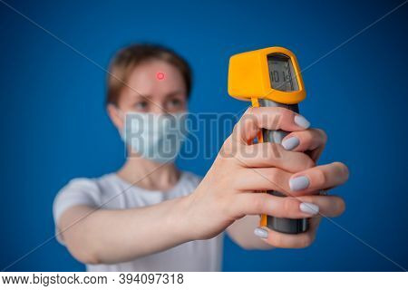 Woman In Medical Face Mask Holding Yellow Pyrometer To Measure Body Temperature - Close Up View, Sel