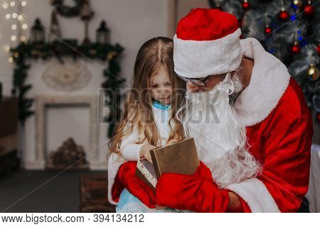 Christmas Gifts For Children. The Little Girl Opens The Gift With Santa Clauss. Gift Box For The Kid
