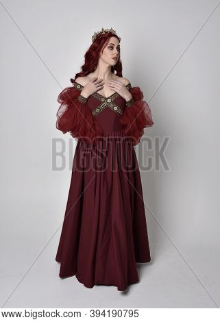 full length portrait of pretty woman wearing red medieval gown with gold crown. Standing pose, again
