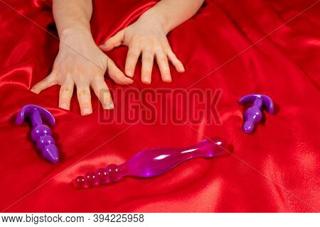 Womens Hands, Anal Dildo On A Red Background. Masturbation And Orgasm, Beautiful Photo For Sex Shop.