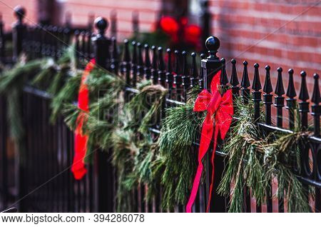 Red Ribbon Bows And Pine Tree Garland Hang On A Black Iron Fence As Outdoor Christmas Holiday Decora