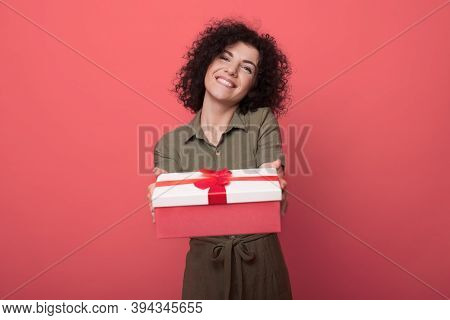 Curly Haired Brunette Woman Is Wearing A Dress And Showing At Camera A Present Smiling Toothily