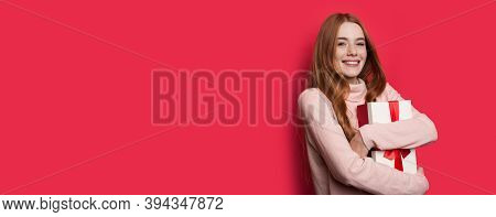 Freckled Woman With Red Hair Is Embracing A Gift And Smile At Camera Near Red Studio Free Space