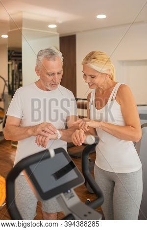 Mature Couple Checking Pulsometers In Gym And Discussing The Results