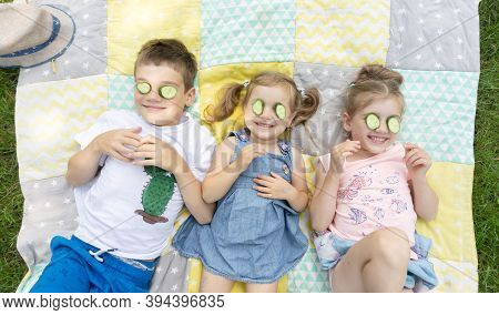 Funny Kids Having Fun During Summer Holidays At Family Camp. Children Try On A Cucumber Mask For Fun