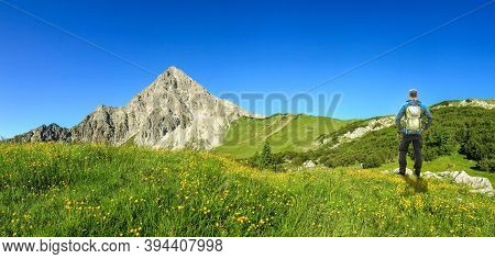 Hiking Man With Backpack On Flower Meadow Enjoying Mountains And Flower In Spring. Geisshorn, Allgau