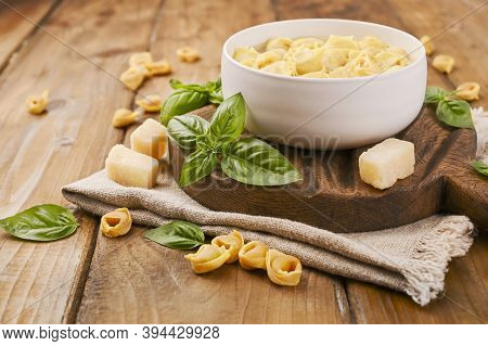 Brodo Soup With Tortellini Mignon On A Wooden Board With Basil And Parmesan. Specialties Of The Cuis
