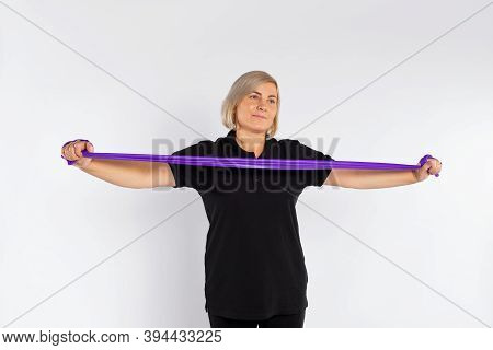 Sporty Senior Woman On A White Background Stretches The Fitness Elastic Band In Her Hands. Healthy L