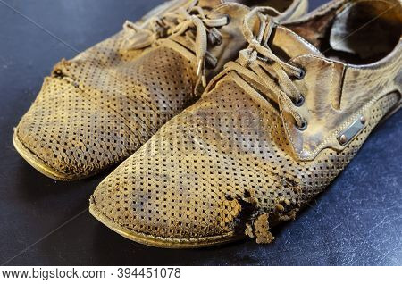 Old Torn Yellow Summer Shoes On A Black Background. A Pair Of Men's Heavily Worn Leather Shoes.