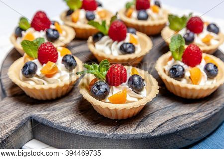 Fruit And Berry Tartlets Dessert Assorted On Wooden Tray. Closeup Of Delicious Pastry Sweets Pies Co