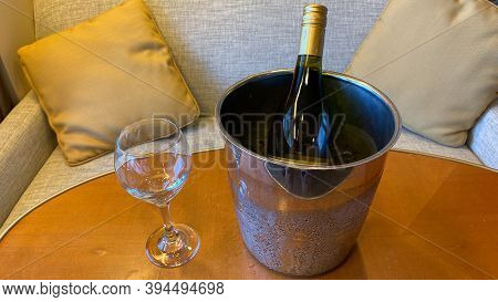 A Bottle Of Wine In An Ice Bucket On A Wooden Table With A Wine Glass Sitting Next To The Bucket.