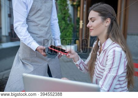 Brown-haired Female Paying Bill With Smartphone In Open Air Cafe